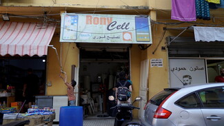 Under a fading sign for “Rony Cell,” a plumber has set up shop for repairs and used appliances. He has been working for several months now, but it is too expensive to put up a new sign; and work has been slow. Today, he made 50,000 L.L., but sometimes he goes for weeks without any business. Nabaa, Lebanon. June 26, 2021. (Mohamad Cheblak/The Public Source)