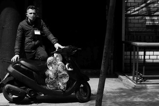 Man wearing a face mask standing by his motorcycle, which carries 6 gallons of oil.
