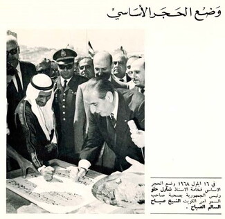 A page from a brochure in Arabic reading "Laying the foundation stone" with an image of President Helou and a smiling Sheikh Al-Sabah as they place their fists on the foundation stone. Dignitaries, at least one in military attire, many in sunglasses, crowd around the leaders, expectantly. 