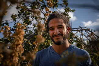 A portrait of a man standing amidst trees and a cloudy sky.