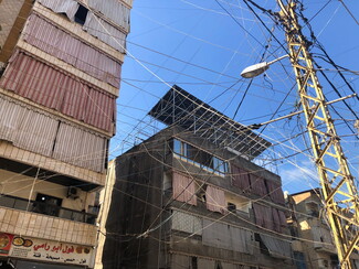 Solar panels can be seen from the street on top of a building. The foreground of the picture shows a street light and an electricity pole that carry dozens of entangled wires.