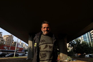 An old man stands in the sun under the otherwise dark Cola bridge.