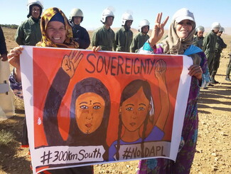 امرأتان تحملان لافتة كتب عليها "#300kmSouth" على أحد الجانبين و"#NoDAPL" على الجانب الآخر. وخلفهم صف من رجال الشرطة.