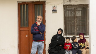“Family Portrait”–Relatives gather beneath the watchful gaze of a martyr as the funeral procession passes by.