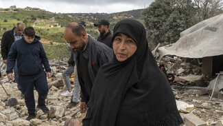 Hajjeh Amal standing in front of the rubbles of the martyred Hussein family's house.