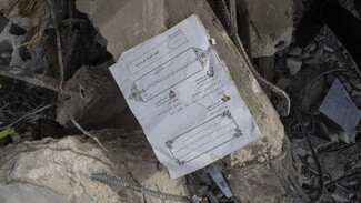 Amidst the rubble, a few surviving pages lay scattered, bearing the title: “How Do I Recognize My Religion?” Beneath the title, a verse from the Quranic chapter ‘The Troops’ stands out against the backdrop of destruction.