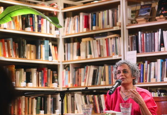 Indian author Arundhati Roy speaks into the microphone at Barzakh Bookshop in Hamra, with a vast array of books visible behind her.