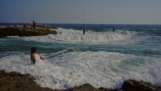 Fishermen standing waiting for their catch while a man swims in the deep water of Dalieh. 