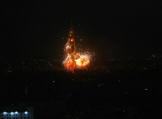 A nighttime airstrike causes an explosion over a dark town.