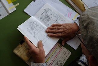 An older man in a cap looks down at documents written in Arabic. 