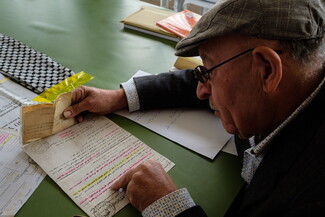 An older man in a cap looks down at documents written in Arabic. 