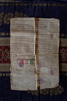 An old, worn document with handwritten text and postage stamps, laid on a patterned cloth.