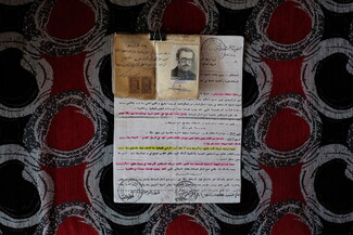 A document and an aged photograph of a man, held together by a paperclip, on a patterned tablecloth.