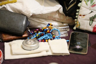 A collection of personal items including a cell phone, wallet, purse, and worry beads on a neutral background.