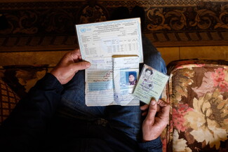 Hands holding Lebanese identification cards and UNRWA registration cards up to the camera.