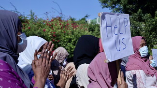 A group of women carrying a sign that reads "HeLP US" as they march.
