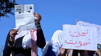 A group of women holding up signs to the camera. One of them reads "We are dying" in Arabic.