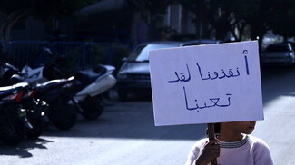 A child holds up a sign in Arabic that reads "Save us, we are tired."