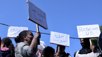 A group of women carrying signs that read "HeLP US," "Save us we are tired," "We are dying," and "Rescue us" as they march.