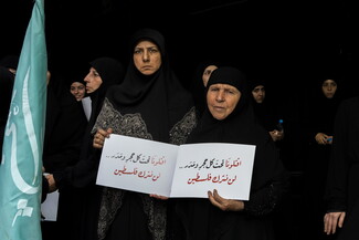 Two veiled women stand facing the camera, other women stand behind them. All are wearing black.