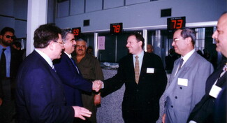 A gathering of men in suits, with two smiling and shaking hands at the center of the photo.