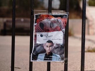  The image of a young man is taped to a gate. The image is split in half: on the top part, the boy is dead, on the bottom he is alive.