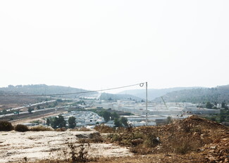 In the foreground, stones and shrubs are visible. Beyond that, there is a maze of buildings with white walls.