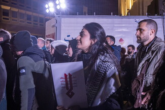 A young woman standing among the crowd in Riad al-Solh Square. She carries an Arabic poster that reads: "No."
