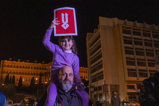 A demonstrator carries his daughter on his shoulders; she carries a poster in Arabic that reads: "No."