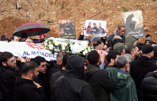 A crowd of mourners carries a coffin draped with an Al Mayadeen flag and covered in white flowers during a funeral in Dahieh, Beirut, while others hold photos of slain journalists, Ali Shoeib, Fatima and Mohammad Ftouni..