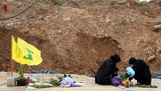 Two women dressed in black sit beside a grave in a mass cemetery in Dahieh, Beirut.