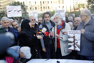 Former militant Georges Abdallah standing among a crowd and speaking into several microphones in front of him.
