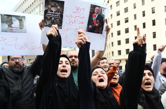 People protest in front of a sign that reads: “Israel is the reason for this country's hardship, not the resistance.” A portrait of Lebanon's president Joseph Aoun is on the poster.