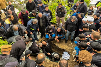 A large group of people gathers solemnly around an open grave during a burial.