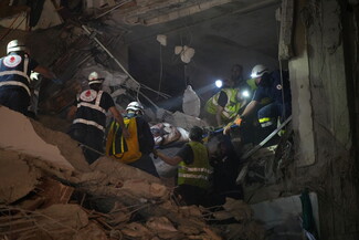 Rescue workers carry a person on a stretcher through rubble at night, using flashlights to navigate the collapsed building debris in Beirut, Lebanon.