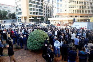 A large crowd gathers in a public square in Beirut. They are surrounded by tall buildings. People appear to be in discussion, conveying a sense of community and engagement.