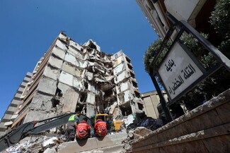 Emergency workers in green and red uniforms assess a severely damaged multi-story buildingin Beirut after an Israeli airstrike.