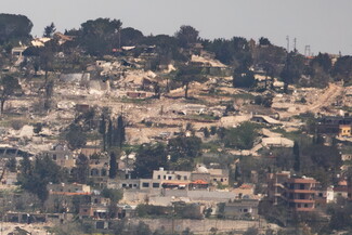 Hillside with scattered, destroyed buildings, rubble, and sparse trees.