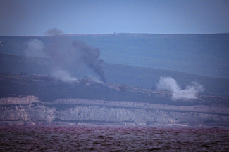 Distant hills with puffs of dark smoke rising into a clear sky.