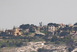 Lebanese village with scattered, damaged and destroyed buildings, rubble, and sparse trees, conveying a sense of destruction and desolation