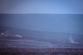 Two locations in distant hills where smoke is rising, appearing to be sites of bombing.