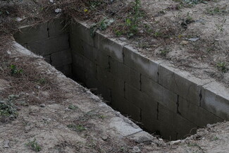 A rectangular grave in the ground, surrounded by dry soil and sparse grass.