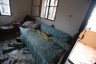A chaotic room with a disheveled blue sofa, scattered debris, and broken windows.