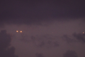A flying object in the sky with two illuminated lights, appearing to be a drone.