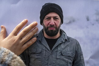 A child's hand on a poster photo of a bearded man wearing a jacket and a beanie. 