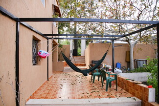 An outdoor patio with a hammock hangs under a pergola. Plastic chairs and a child's swing are nearby.