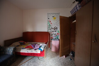 Small bedroom with a single bed covered in a colorful blanket, clothes scattered on top.