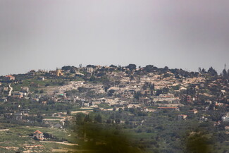 A hilly landscape featuring destroyed scattered houses amidst lush greenery.