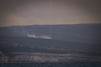 Smoke rises from a Merkava tank after being targeted in the distance, set against hills and greenery.