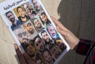 Hands holding a poster bearing photos of Lebanese abductees held in Israeli prisons.
